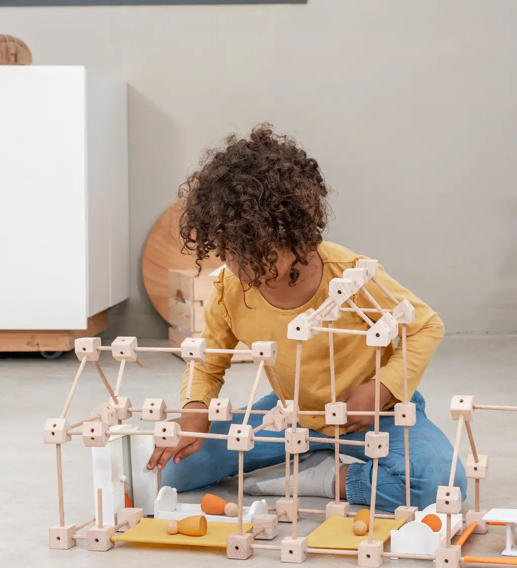 A child building a house using various wooden poles and blocks from the Trigonos mini large construction set 