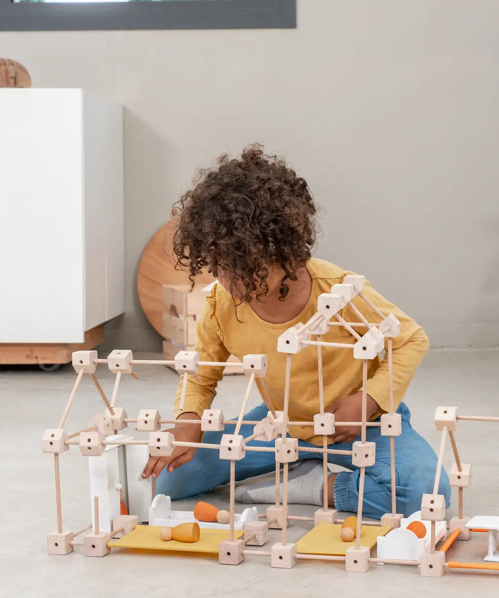 A child building a house using various wooden poles and blocks from the Trigonos mini large construction set 
