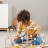 A child building a house using various wooden poles and blocks from the Trigonos mini large construction set 