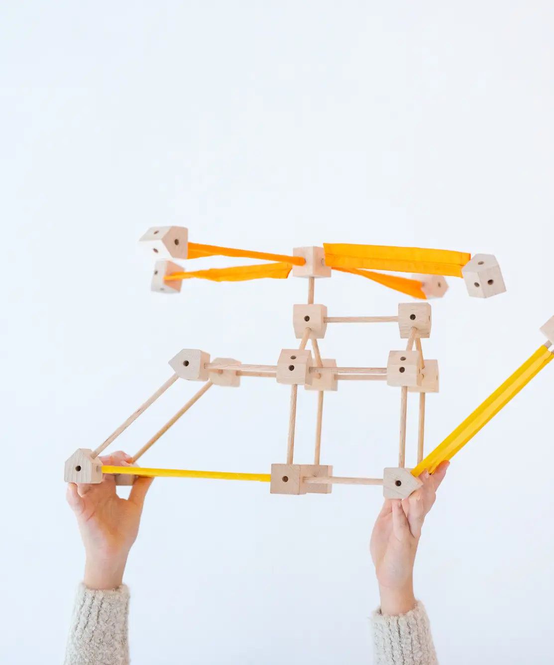 A child holding up a helicopter made from various wooden poles and blocks out of the Trigonos mini large construction set 