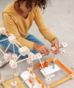 A child building using various wooden poles and blocks from the Trigonos mini large construction set on a concrete surface