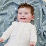 A baby lying flat on the blue MORI muslin square showing the cute white prints of clouds, stars and the moon on organic cotton fabric