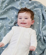 A baby lying flat on the blue MORI muslin square showing the cute white prints of clouds, stars and the moon on organic cotton fabric