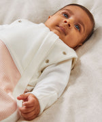 A close up of a baby laid on a soft surface inside the blush stripe MORI swaddle. Showing the popper detail on the arms, and design detail