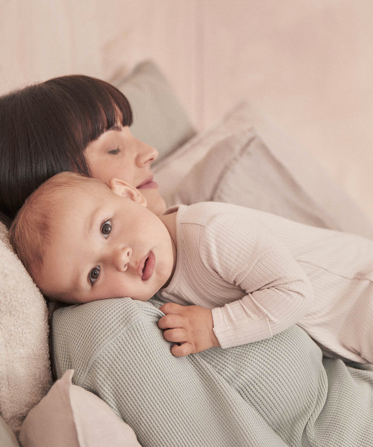 A close up of a baby resting on the mothers shoulder wearing the MORI ecru two way sleepsuit showing the ribbed detail