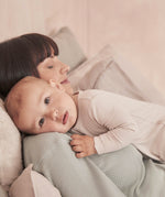 A close up of a baby resting on the mothers shoulder wearing the MORI ecru two way sleepsuit showing the ribbed detail