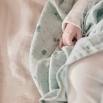A close up of the grey MORI muslin square with a baby hand showing the cute dark grey print detail of clouds, stars and the moon on soft organic cotton fabric