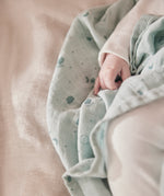 A close up of the grey MORI muslin square with a baby hand showing the cute dark grey print detail of clouds, stars and the moon on soft organic cotton fabric