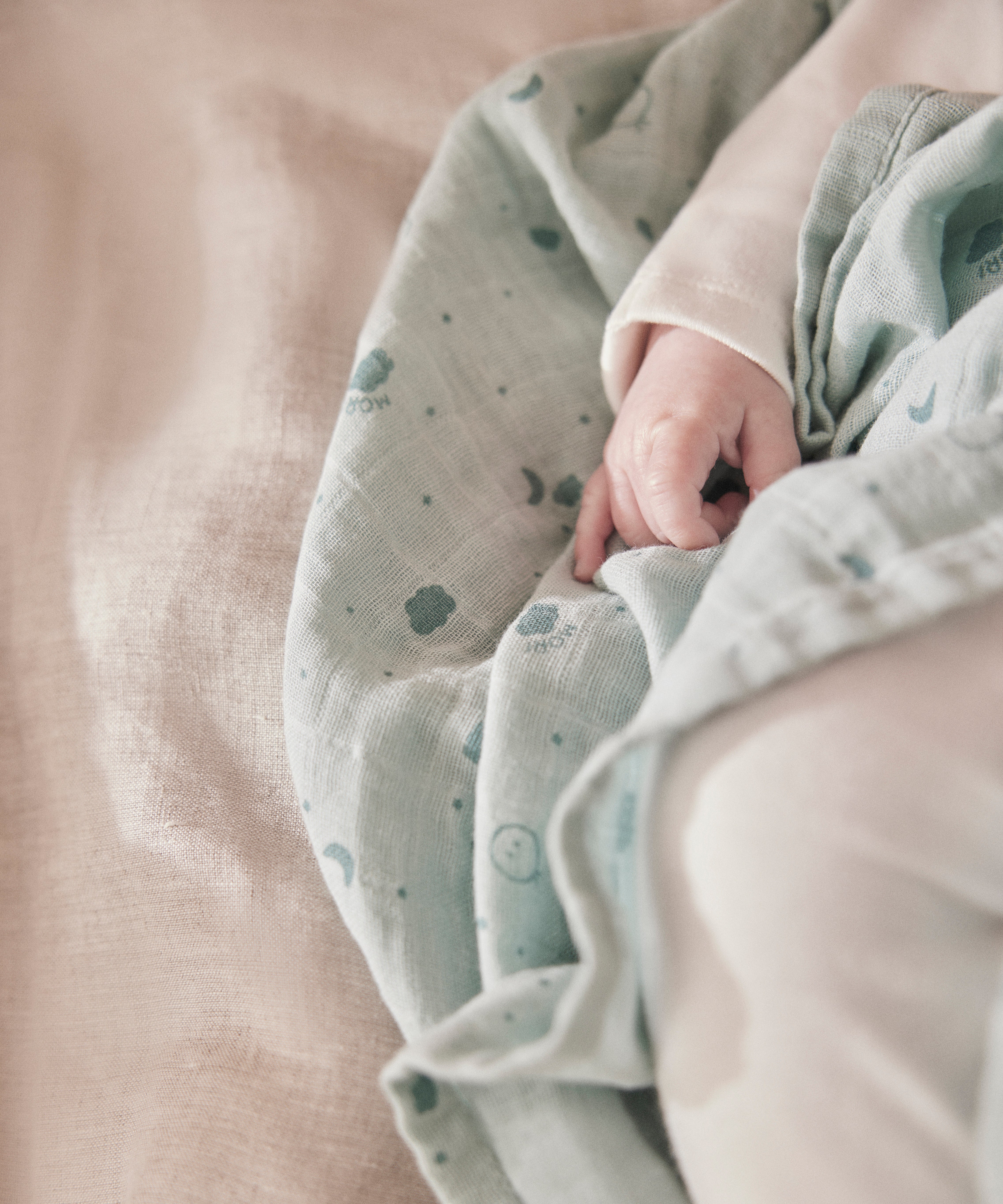 A close up of the grey MORI muslin square with a baby hand showing the cute dark grey print detail of clouds, stars and the moon on soft organic cotton fabric