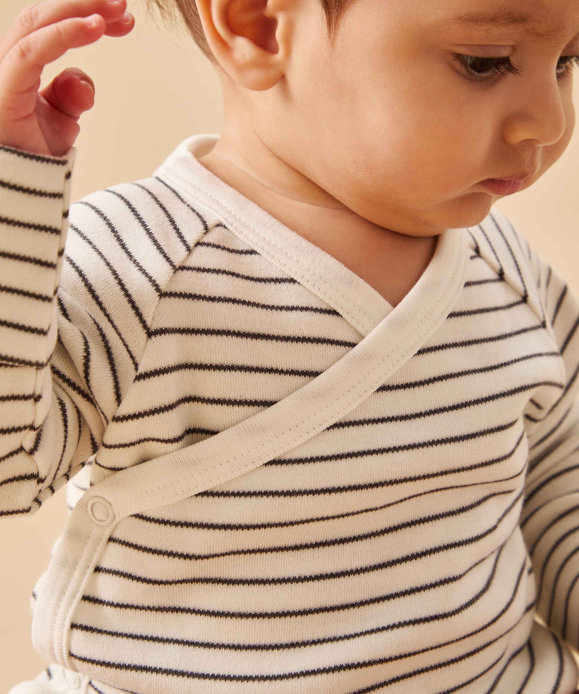 A closeup of a mori organic baby kimono bodysuit, in white with a grey stripy design, worn by a baby