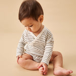 A baby sat upright, wearing a mori organic baby kimono bodysuit, in white with a grey stripy design