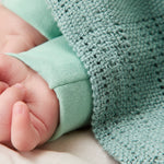 A close up of the MORI mint cellular blanket with a baby hand showing the air hole detail for temperature control