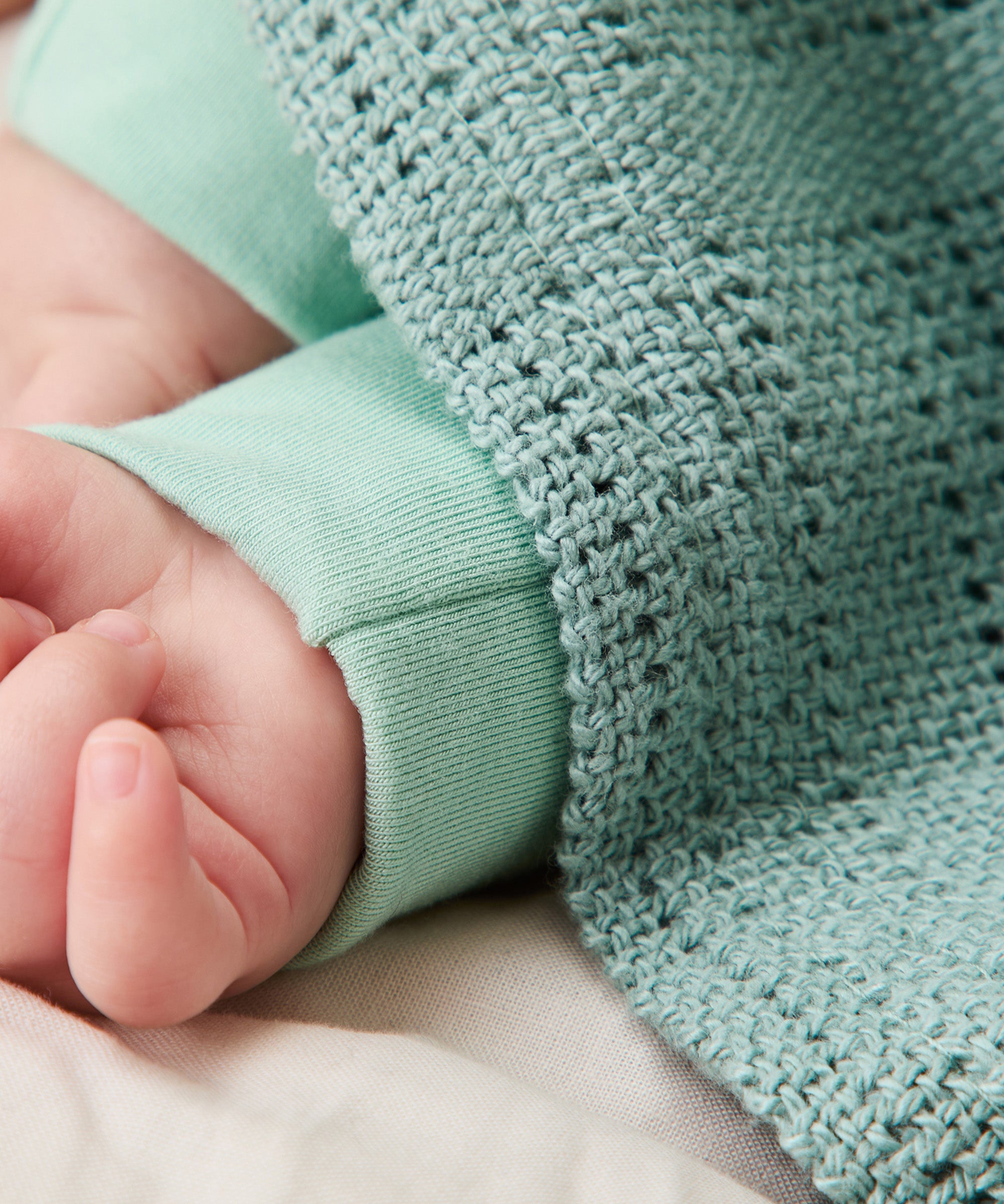 A close up of the MORI mint cellular blanket with a baby hand showing the air hole detail for temperature control