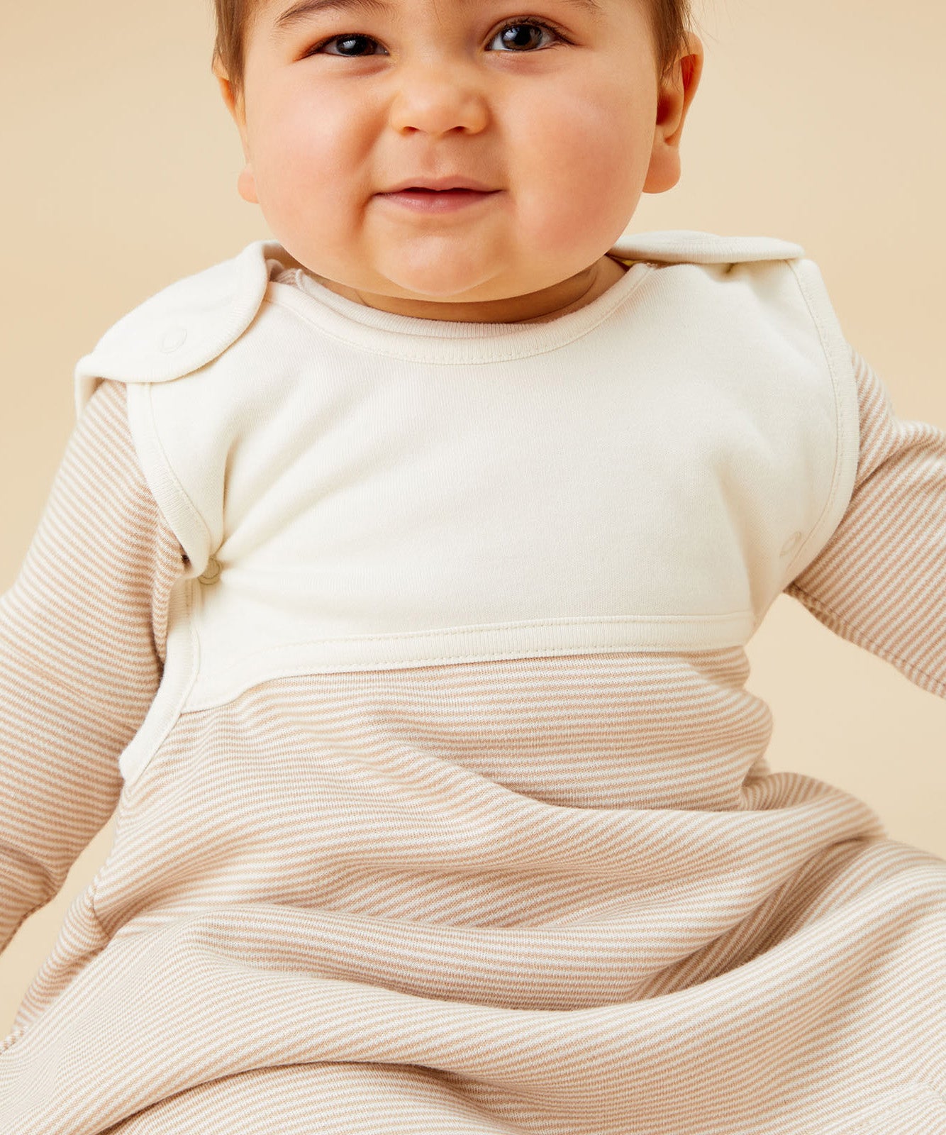  A baby inside the oatmeal sriped MORI sleeping bag showing the stripe detail on organic cotton fabric and popper fastener on the shoulder for easy fitting 