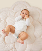 A little baby laying on a flower-shaped mat, wearing the Mori organic kimono baby bodysuit in white.