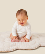 A baby sitting up and laughing, wearing the Mori organic kimono baby bodysuit in white.