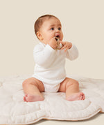 A baby sitting up and wearing the Mori organic kimono baby bodysuit in white.
