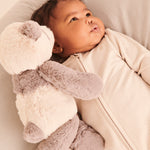 A little baby wearing the Mori clever zipped sleepsuit in Ecru white, and cuddling a teddy bear
