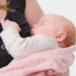 A little baby being held in a woman's arms, wearing the Mori clever zipped sleepsuit in Ecru white