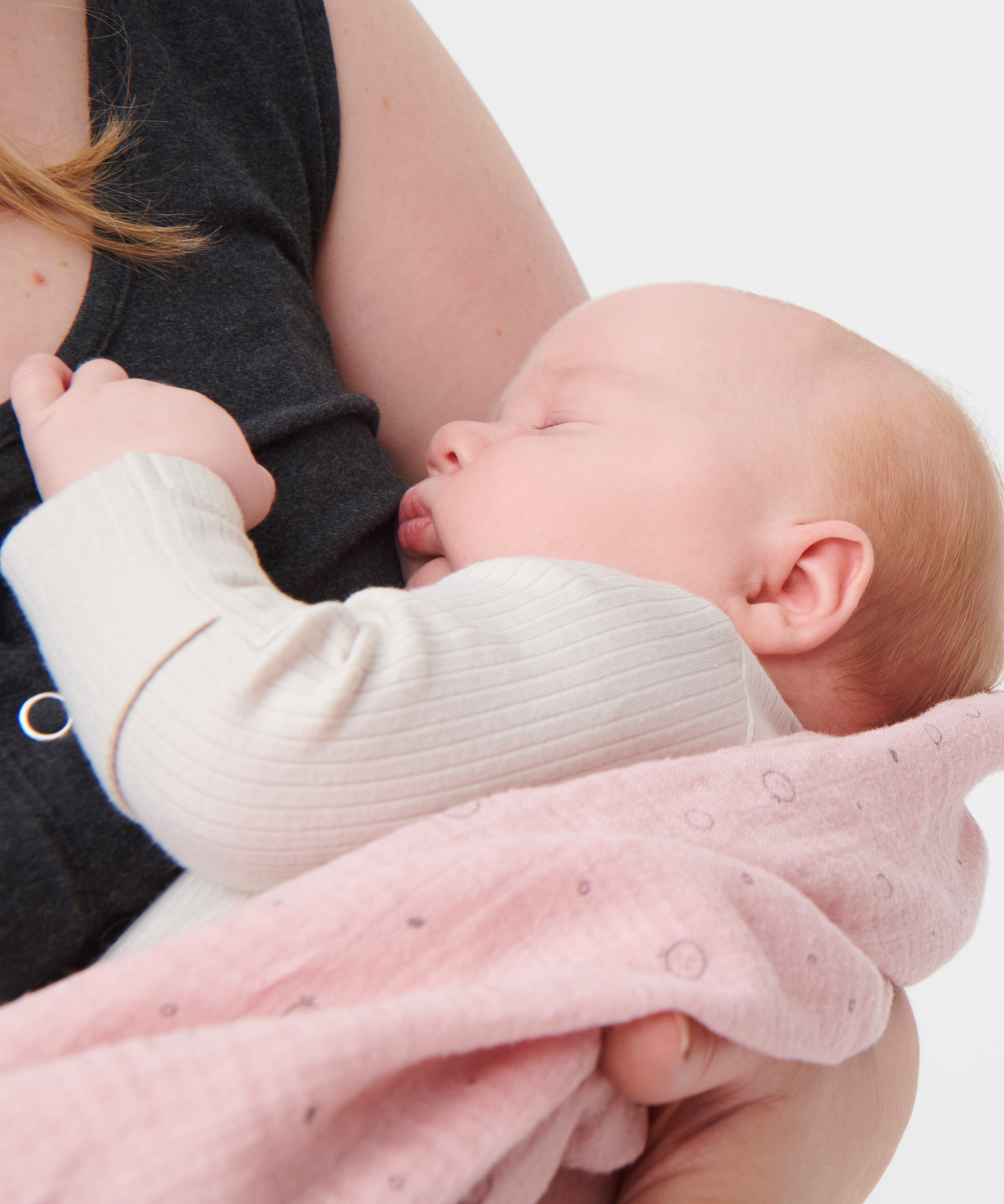 A little baby being held in a woman's arms, wearing the Mori clever zipped sleepsuit in Ecru white
