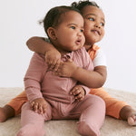 A little baby wearing a rose coloured Mori clever sleepsuit, being hugged by her older toddler sister