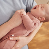 A closeup of a yawning newborn baby being held, wearing a rose coloured Mori clever sleepsuit