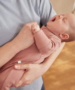 A closeup of a yawning newborn baby being held, wearing a rose coloured Mori clever sleepsuit