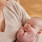 A little baby being held in a woman's arms, wearing a rose coloured Mori clever sleepsuit
