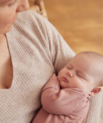 A little baby being held in a woman's arms, wearing a rose coloured Mori clever sleepsuit