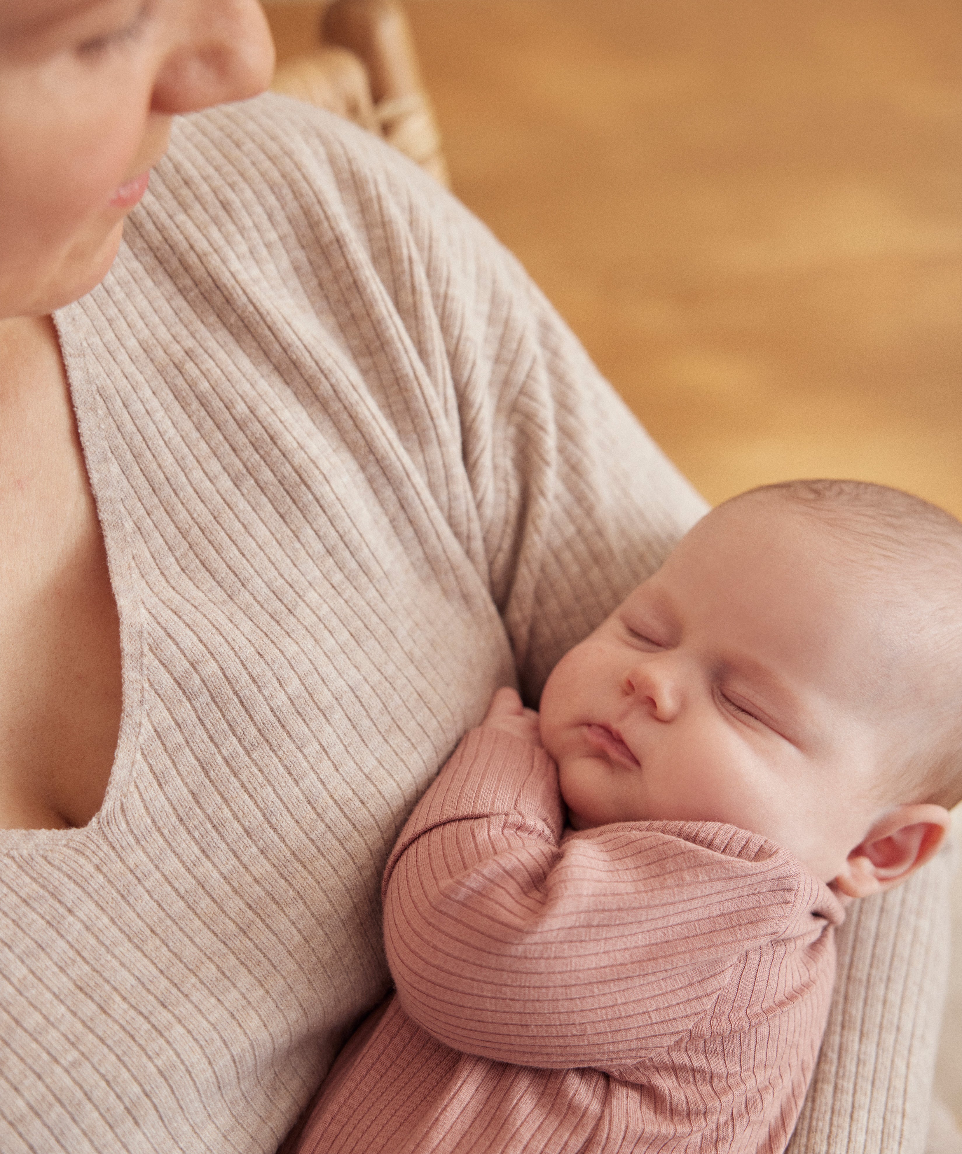 A little baby being held in a woman's arms, wearing a rose coloured Mori clever sleepsuit