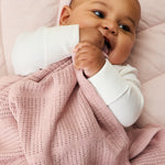 A close up of a baby clutching the rose MORI cellular blanket showing the air hole detail for temperature control