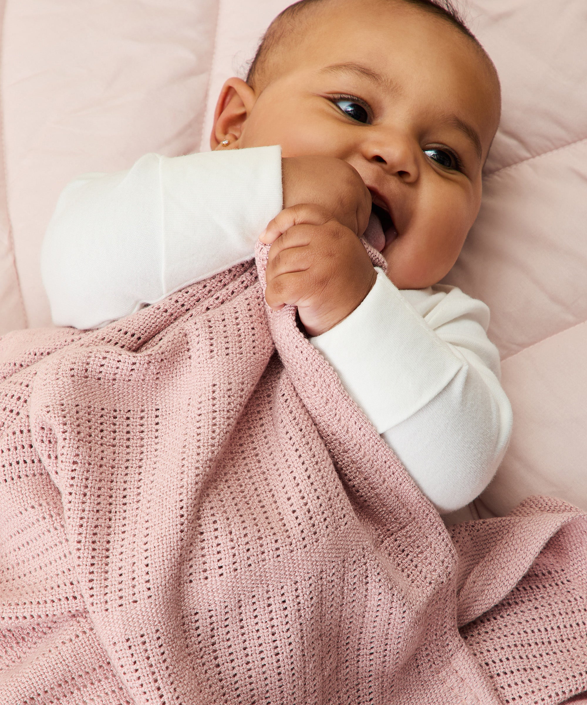A close up of a baby clutching the rose MORI cellular blanket showing the air hole detail for temperature control