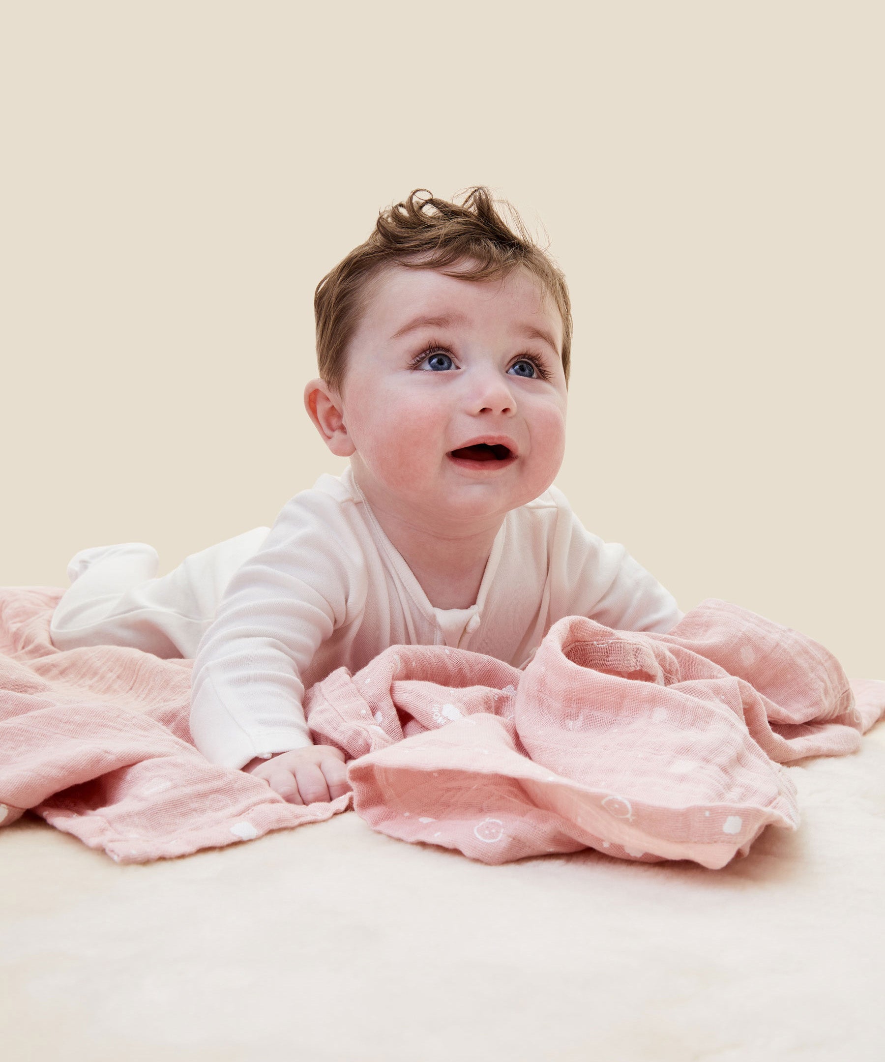 A baby crawling on the pink MORI muslin square showing the cute white prints of clouds, stars and the moon on organic cotton fabric