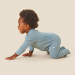 A crawling baby wearing the Mori organic zip sleepsuit in a sky blue colour
