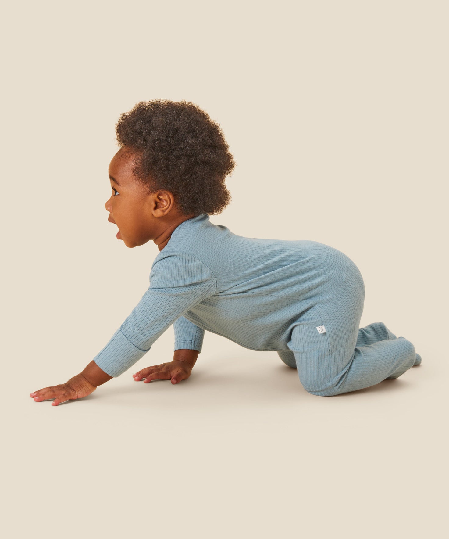 A crawling baby wearing the Mori organic zip sleepsuit in a sky blue colour