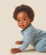 A crawling baby wearing the Mori organic zip sleepsuit in a sky blue colour