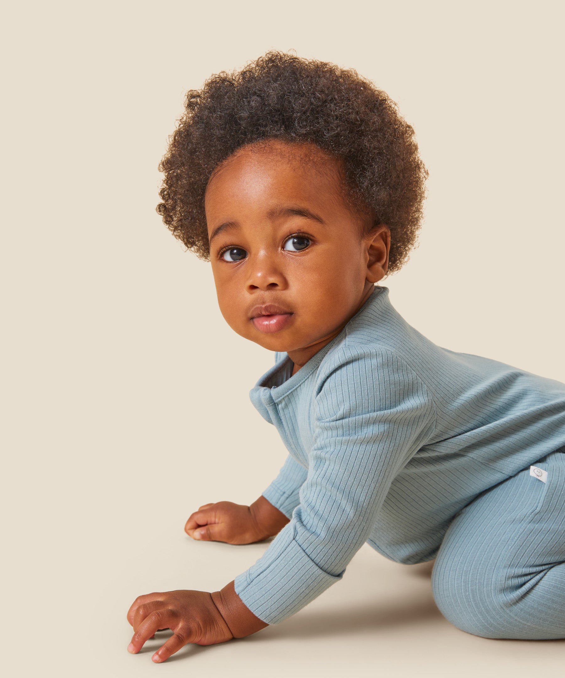 A crawling baby wearing the Mori organic zip sleepsuit in a sky blue colour