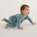 A smiling, crawling, baby wearing the Mori organic zip sleepsuit in a sky blue colour