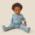 A baby wearing the Mori organic zip sleepsuit in a sky blue colour