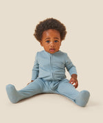 A baby wearing the Mori organic zip sleepsuit in a sky blue colour