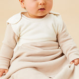 A baby sitting inside the oatmeal sriped MORI sleeping bag showing the popper fastener on the shoulder for easy fitting. 