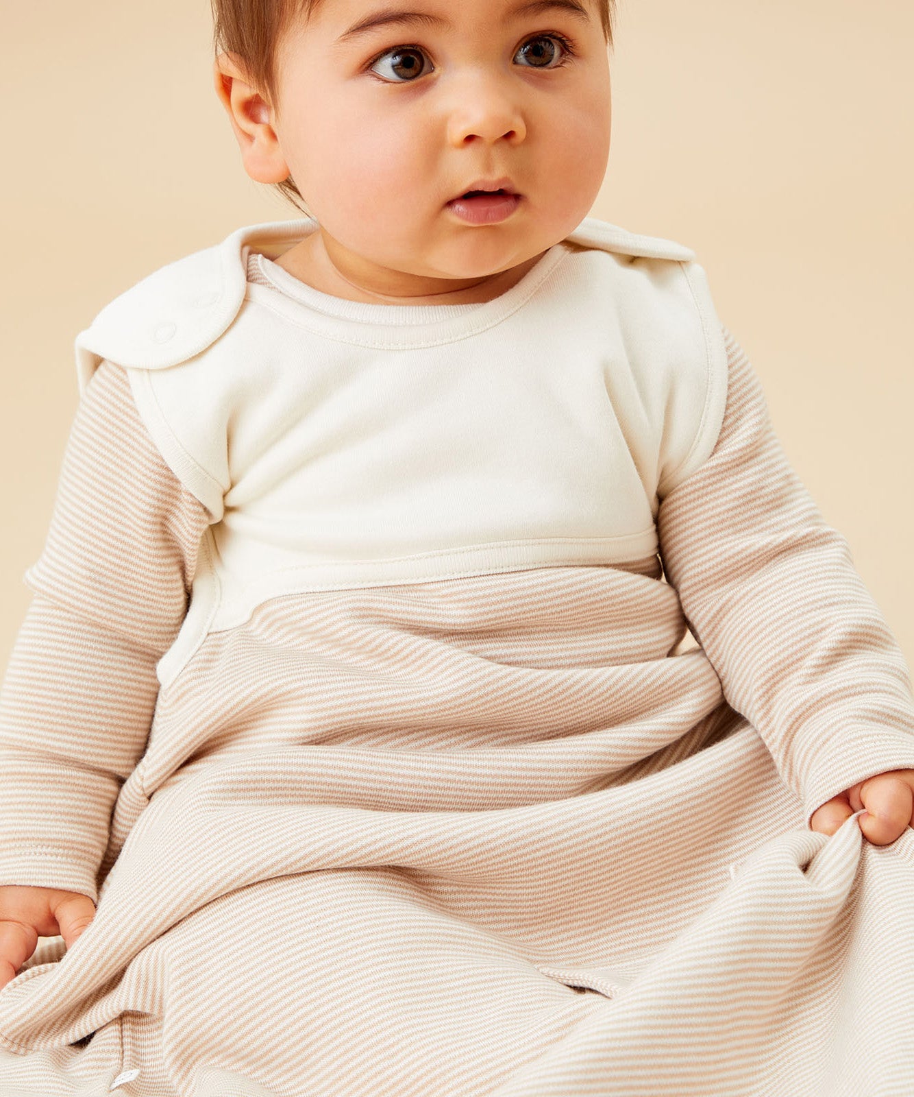 A baby sitting inside the oatmeal sriped MORI sleeping bag showing the popper fastener on the shoulder for easy fitting. 