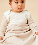 A baby sitting inside the oatmeal sriped MORI sleeping bag showing the popper fastener on the shoulder for easy fitting. 