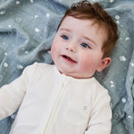 A close up of a baby lying flat on the blue MORI muslin square showing the cute white prints of clouds, stars and the moon on soft organic cotton fabric