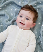 A close up of a baby lying flat on the blue MORI muslin square showing the cute white prints of clouds, stars and the moon on soft organic cotton fabric