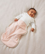 A baby laid on a soft surface inside the blush stripe MORI swaddle. Made from bamboo and organic cotton and features poppers on the arms, to tuck the arms in or let them be free.