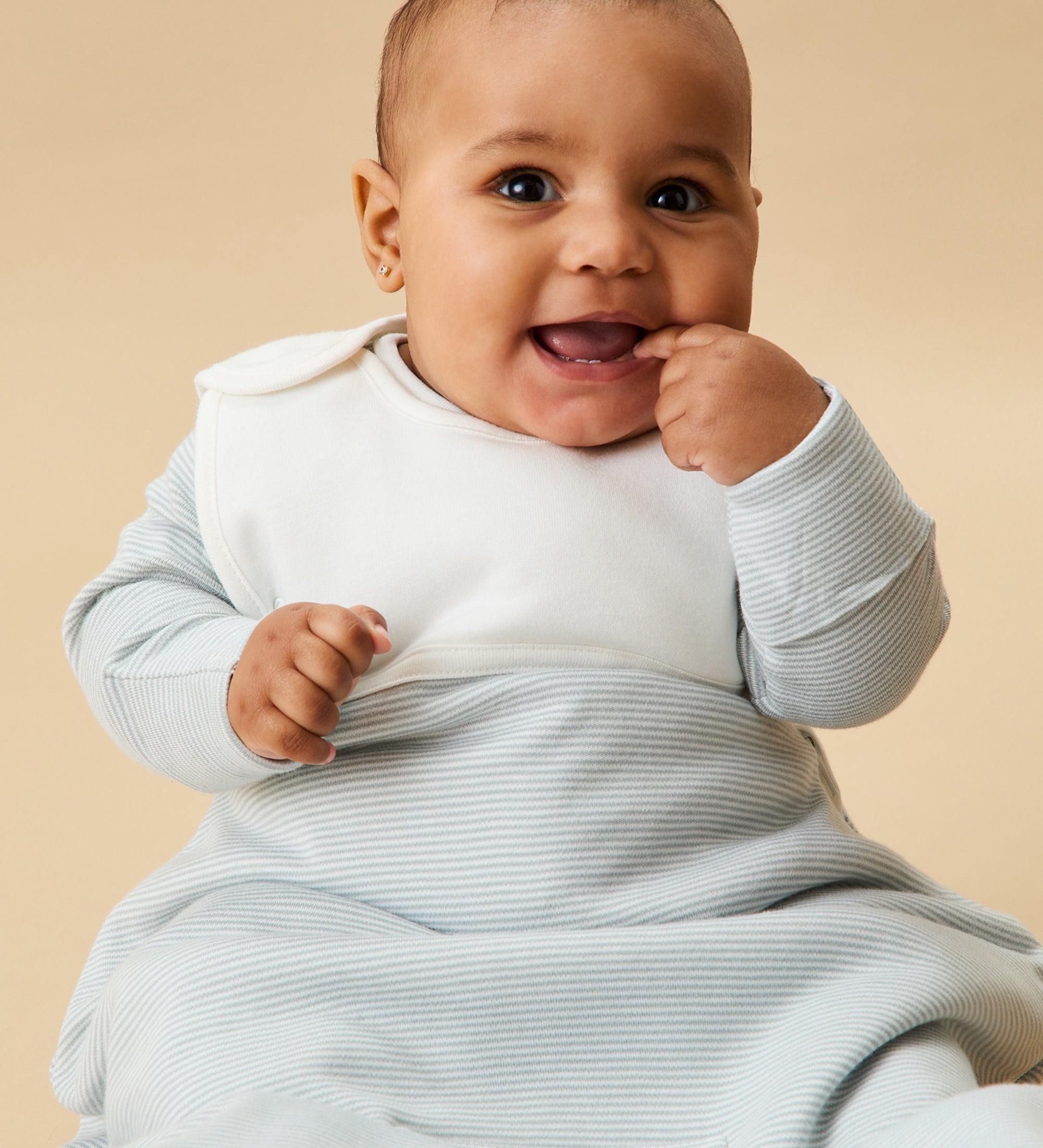 A little baby wearing the Mori organic cotton clever sleeping bag 2.5 TOG, in a blue stripe design.