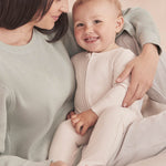 A baby wearing the Mori two way zipped sleepsuit in ecru colour showing the ribbed and zip detail on organic fabric.