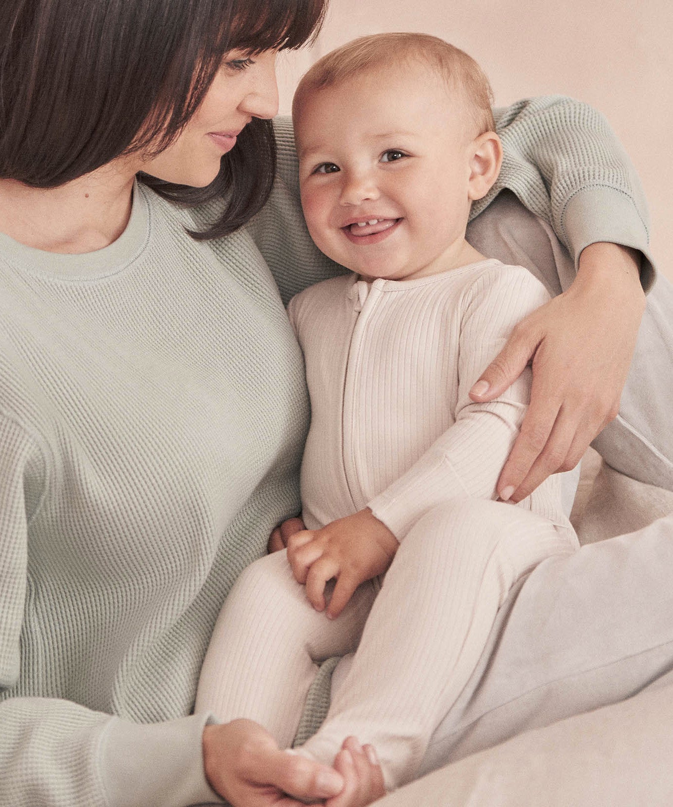 A baby wearing the Mori two way zipped sleepsuit in ecru colour showing the ribbed and zip detail on organic fabric.