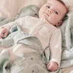 A baby lying flat on the grey MORI muslin square showing the cute dark grey prints of clouds, stars and the moon on soft organic cotton fabric